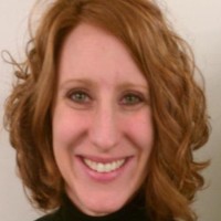Portrait of a smiling woman with curly red hair, likely a researcher or professional in oncology.